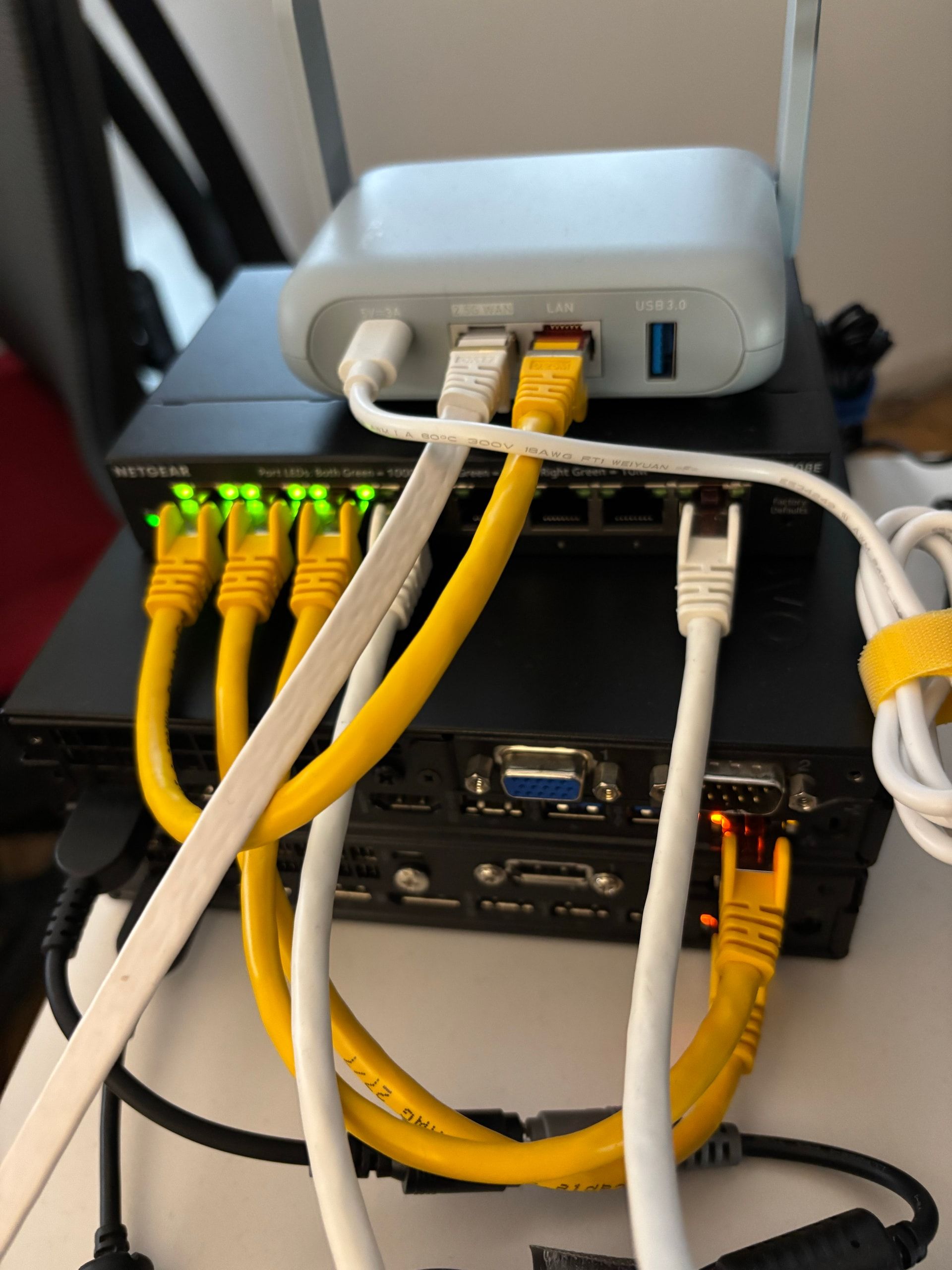 Vue arrière du homelab : routeur GL.iNet, switch Netgear et deux mini-PC Lenovo reliés par Ethernet